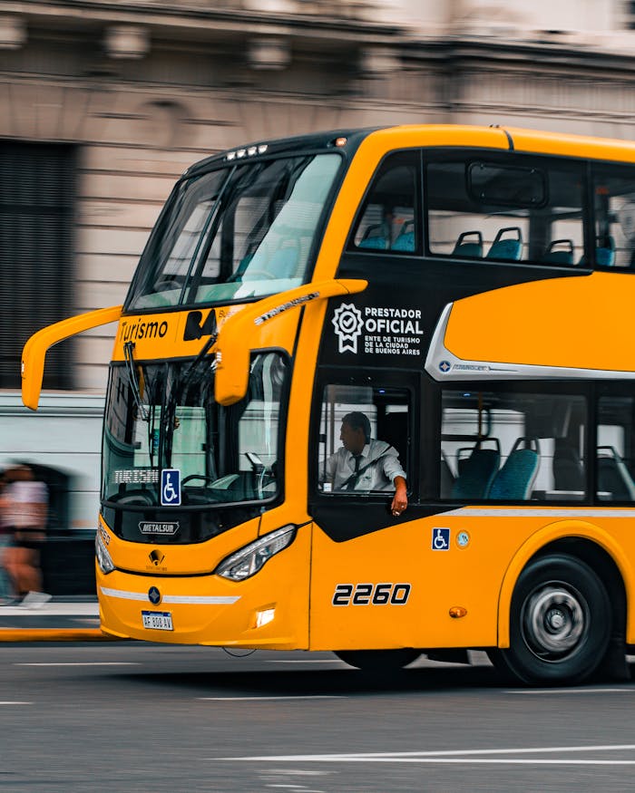 A yellow double-decker tour bus with official markings, driving in Buenos Aires city.